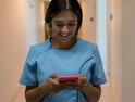 Latin american nurse walking through the hospital's corridor chatting on her smartphone smiling very happy