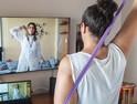 oman watching and copying exercises with a resistance band in her living room, guided by a physical therapist online